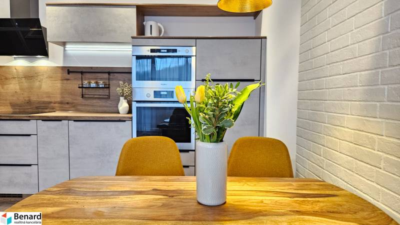 A kitchen in a studio apartment with a wooden decor, a flower vase on the table, yellow chairs.