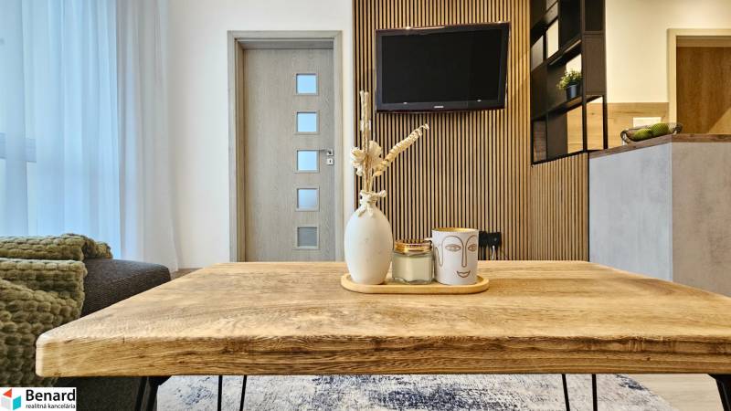Living area of a studio apartment with a wooden table and decorations in the background with a television.