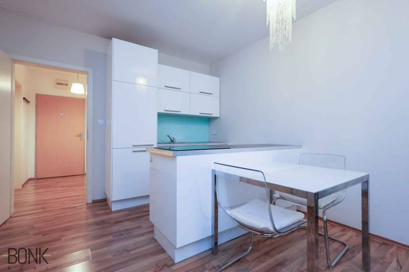 A kitchen in a 2-room apartment with white cabinets and a wooden decor floor.