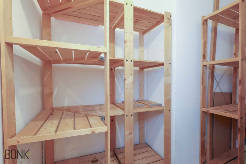 Wooden shelves in the pantry of a two-room apartment with white walls.