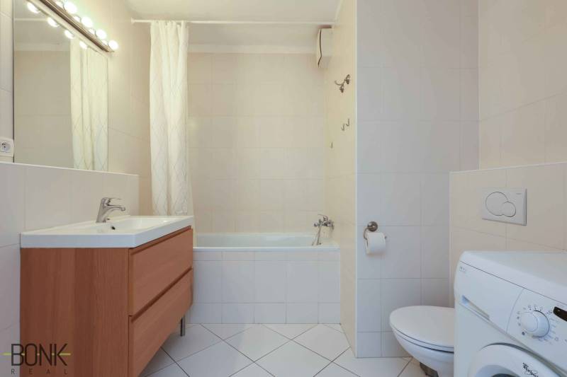 Bathroom with a bathtub, sink, cabinet, toilet, and washing machine in a 2-room apartment.
