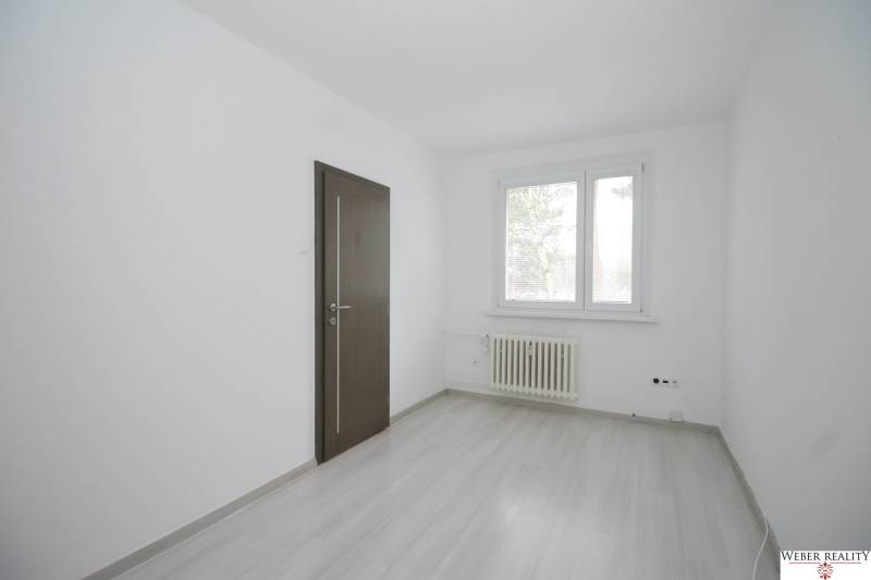 A room in a 3-room apartment with white walls, a wooden decor floor, and a window.
