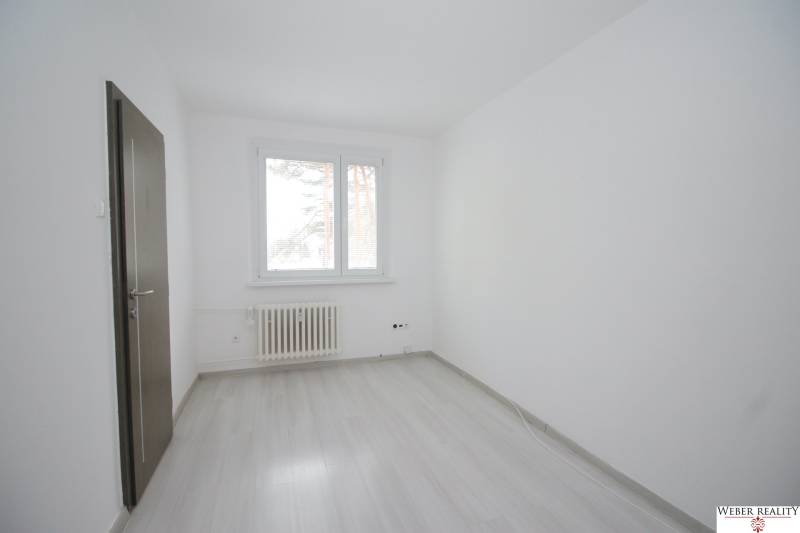 A room with a window, a radiator, and a wooden decor floor in a 3-room apartment.