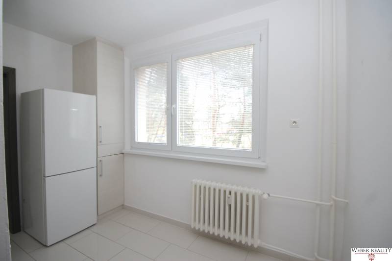 A room in a 3-room apartment with white walls, a radiator, and a refrigerator.