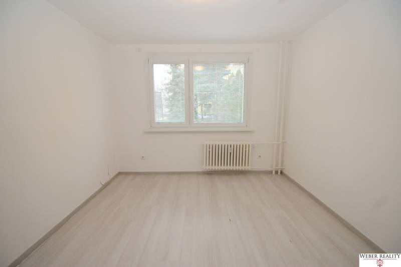 A room with white paint, a window with blinds, and a floor with wood decor in a 3-room apartment.