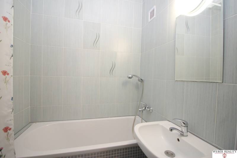 Bathroom in a 3-room apartment with a bathtub, sink, and mirror, light tiles.