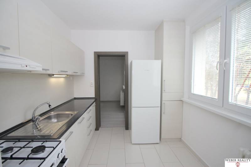 A kitchen with a white unit in a 3-room apartment, large window, refrigerator.