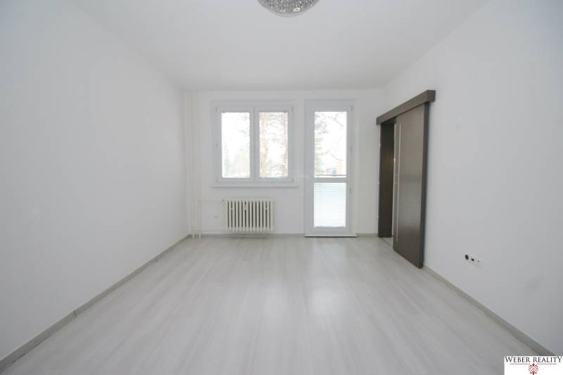 A spacious white room with a wood-patterned floor and a large window in a 3-room apartment.