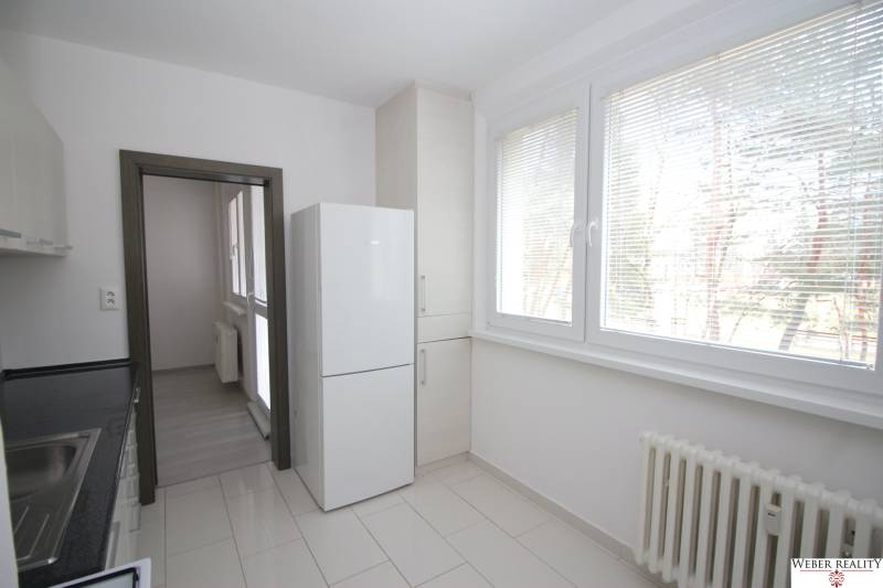 A kitchen in a 3-room apartment with large windows, a refrigerator, and light-colored tiles.