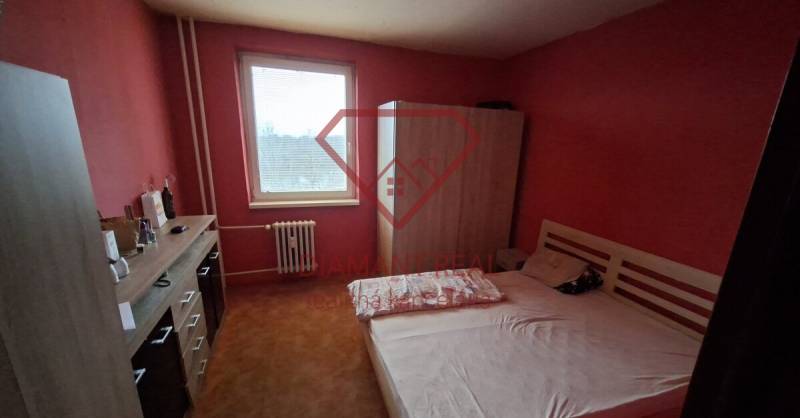 A bedroom in a 3-room apartment with a bed, wardrobe, and dresser on a red wall.