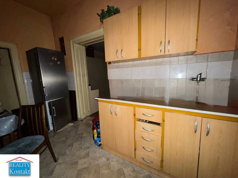 A kitchen in a family house with a refrigerator, cabinets, and a tiled floor.