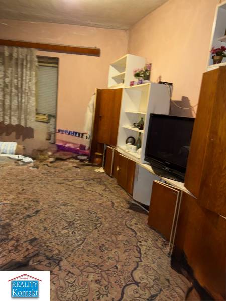 A room in a family house with a carpet, shelves, a television, and curtains.