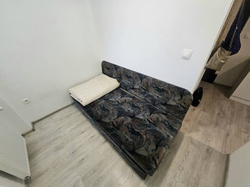 A sofa in a one-room apartment with a wooden decor floor.