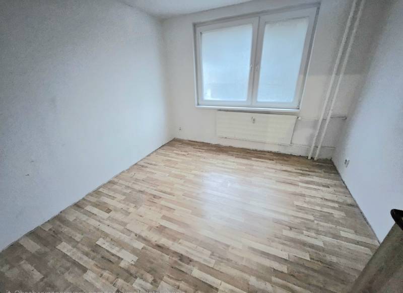 An empty room with white walls and a wooden-patterned floor in a three-room apartment.
