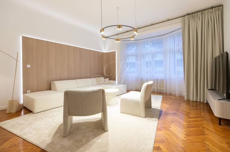 Living room in a three-room apartment with a wooden decor floor, beige carpet, and seating.