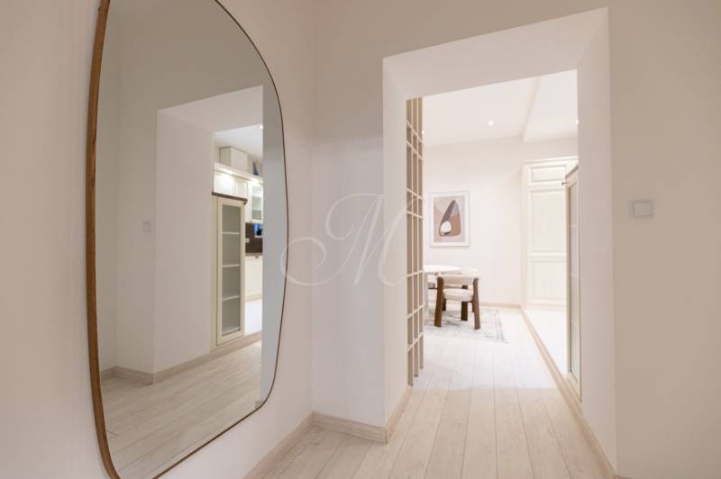 A hallway with a mirror and a view into the kitchen in a 3-room apartment with a wooden decor floor.