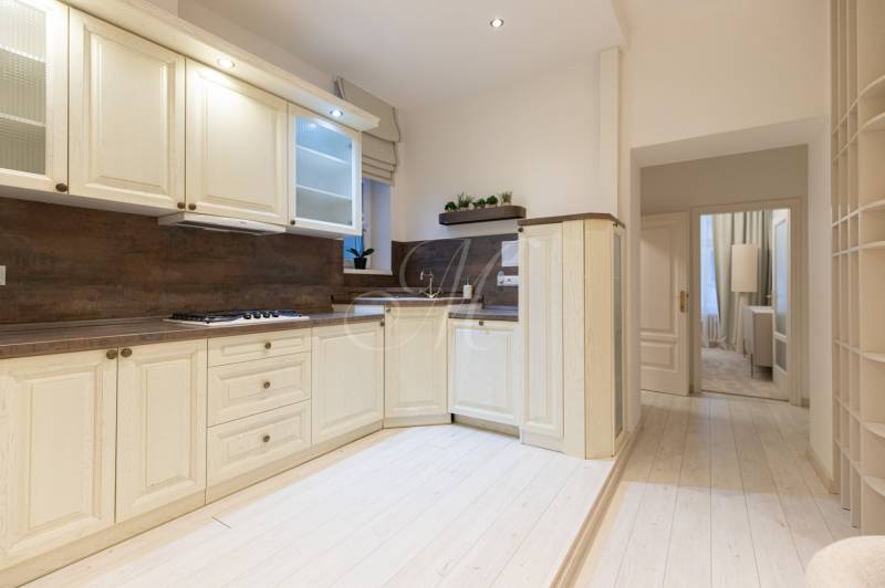 A kitchen in a 3-room apartment with a wood-patterned floor and light-colored furniture.