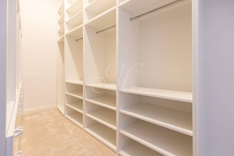 Spacious wardrobe with white shelves and hanging rods in a 3-room apartment.