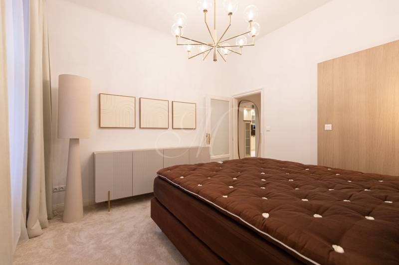 A bedroom with a brown bed, white furniture, and a light fixture in a 3-room apartment.