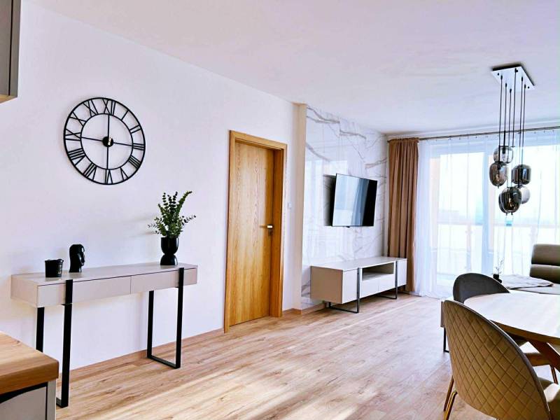 Living room in a three-room apartment with a wooden decor floor, table, and television.