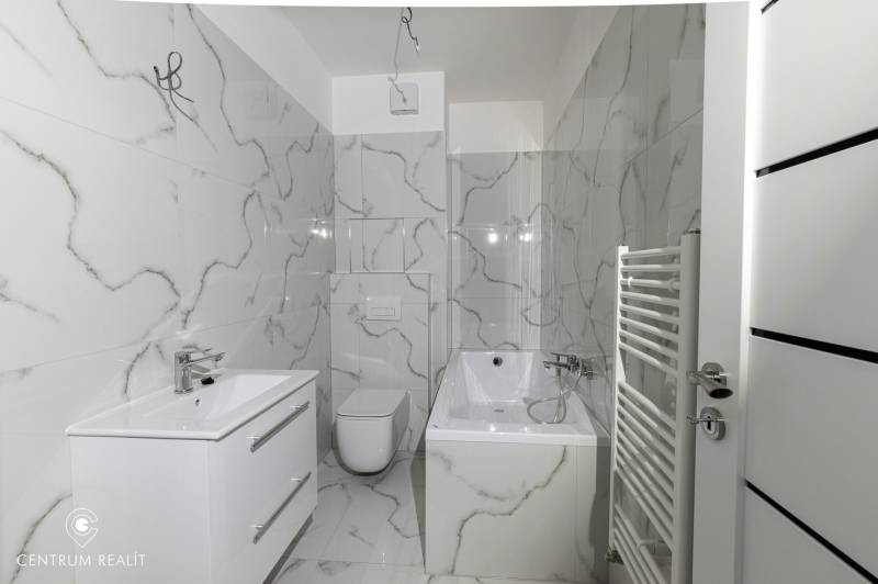 A bathroom with marble decor walls, a bathtub, and a sink in a 2-room apartment.