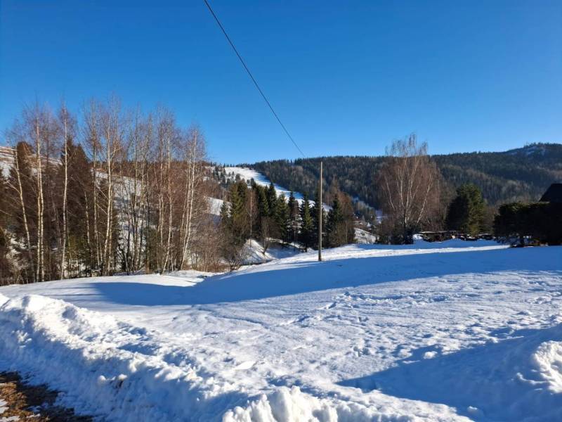 Snow-covered residential plots in Ždiar, surrounded by forests and mountains.