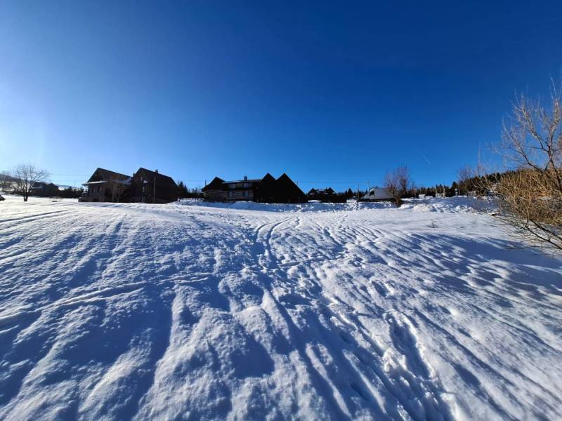 Snow-covered lands in Ždiar with visible houses in the background, clear blue sky.