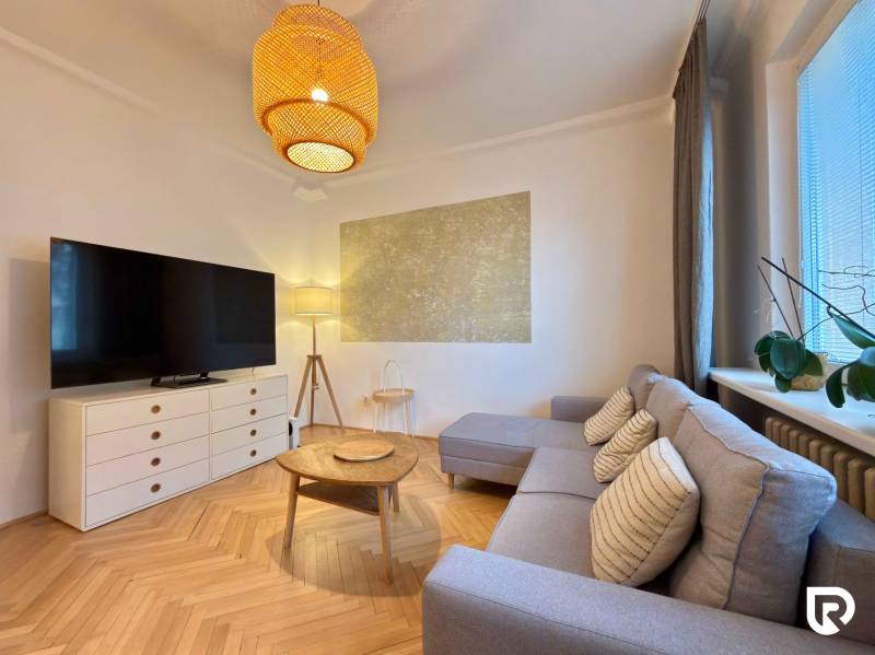 Living room in a two-room apartment with a wooden decor floor, a sofa, and a TV.