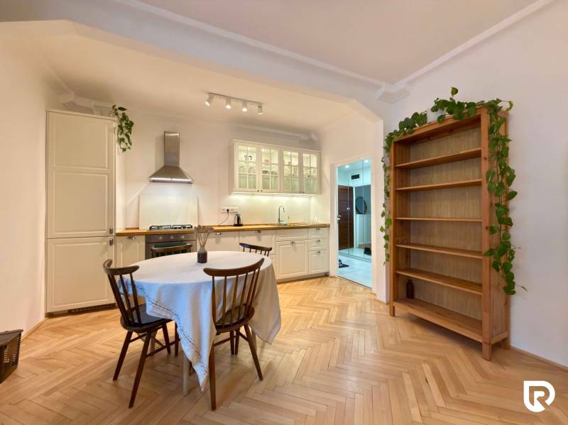 A kitchen in a 2-room apartment with a wooden decor floor, dining table, and shelf.