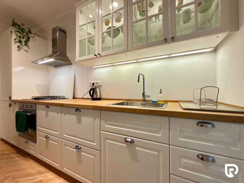A bright kitchen in a 2-room apartment with a wood-patterned floor and white cabinets.