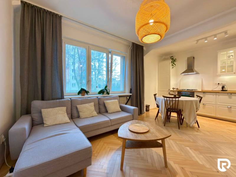Living room with kitchen and dining table, wooden decor flooring, light-colored sofa.