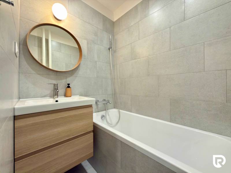 Bathroom with a bathtub in a 2-room apartment, a mirror, and a backlit washbasin cabinet.