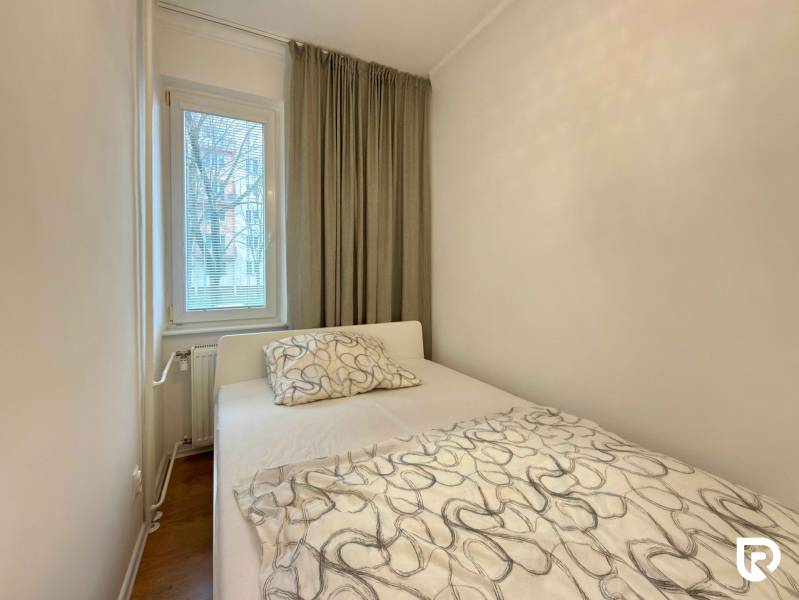 Bedroom in a 2-room apartment with a bed, window, and curtains, floor with wooden decor.