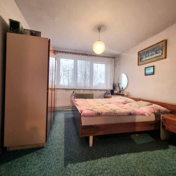 Bedroom in a 3-room apartment with a double bed, carpet, furniture, and curtains on the window.