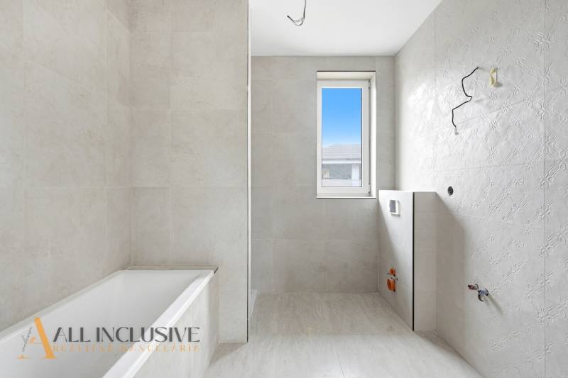 Bathroom in a family house with a bathtub, window, and light tiles.