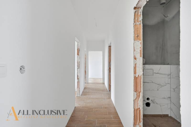 A hallway in a family house with white walls and a wooden-patterned floor.