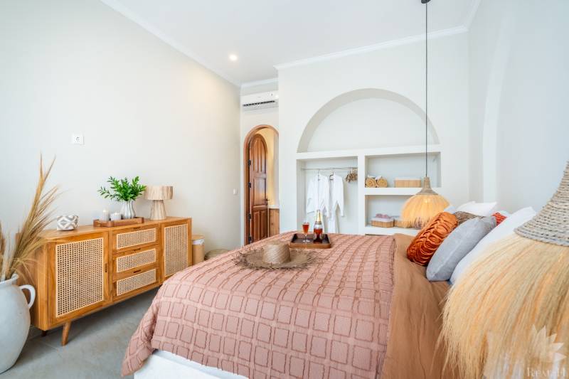 A bright bedroom in a villa with natural decorations, soft lighting, and a comfortable bed.