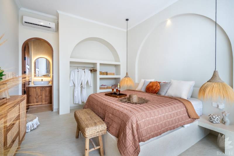 Bright bedroom in a villa with a double bed, lamp, and open wardrobe.