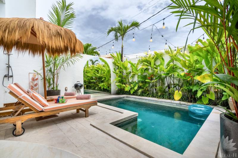 A villa pool with loungers, a rattan roof, surrounded by tropical plants.