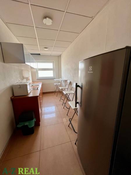 A narrow kitchenette with linoleum flooring, a refrigerator, and a window in office spaces.