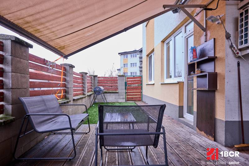 Terrace in a 2-room apartment with a wooden decor floor, outdoor seating, and an awning.
