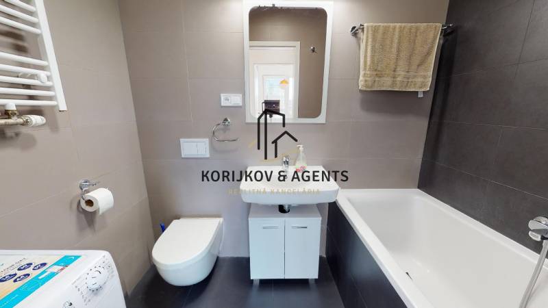 Bathroom with a bathtub, sink, wall-mounted toilet, and washing machine in a 2-room apartment.