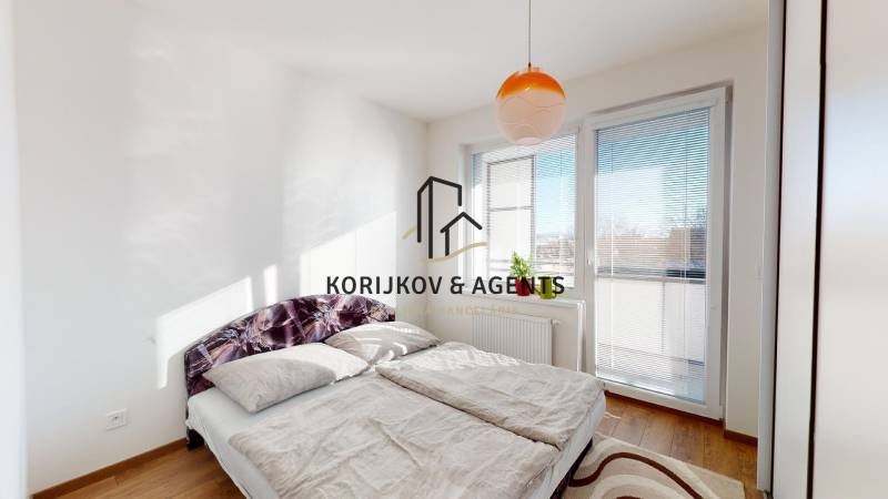 A bright bedroom with a large bed, a window, and a wooden decor floor in a 2-room apartment.