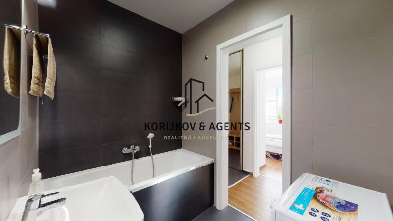 Bathroom in a two-room apartment with a bathtub and a washing machine, floor with wood decor.