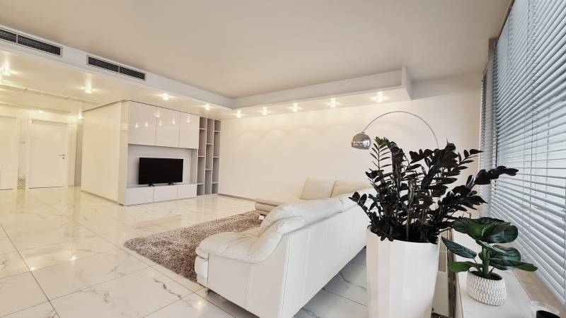 Living room in a 3-room apartment with a white couch, plants, and a TV on a light floor.