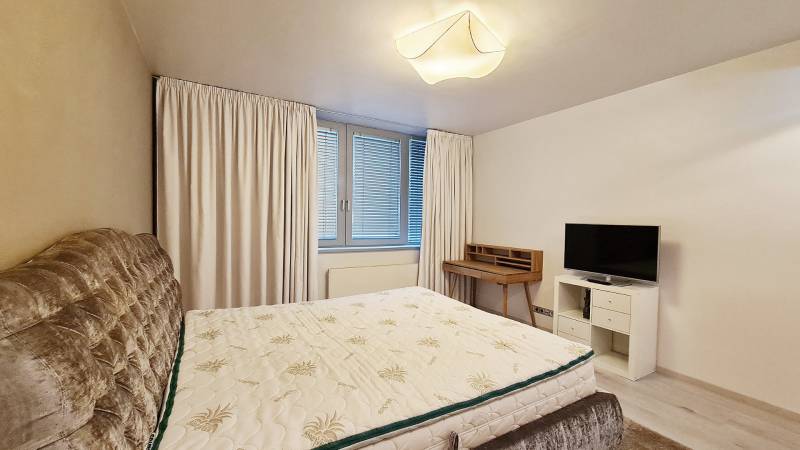 A bedroom in a three-room apartment with a bed, a television, and a writing desk.