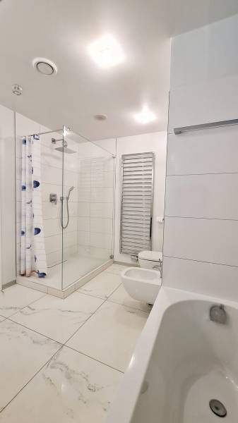 Bathroom with a bathtub, shower, and toilet in a three-room apartment. White tiles.