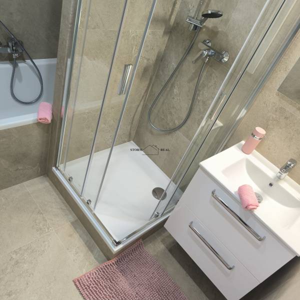 A bathroom in a 4-room apartment with a bathtub, shower, and light tiles.