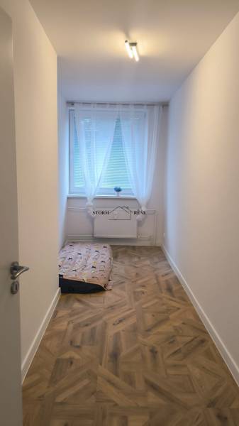 A narrow room with a large window and a wooden decor floor in a 4-room apartment.