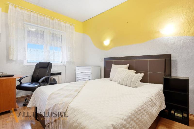 A bedroom in a family house with a bed, an armchair, and a floor with a wooden decor.